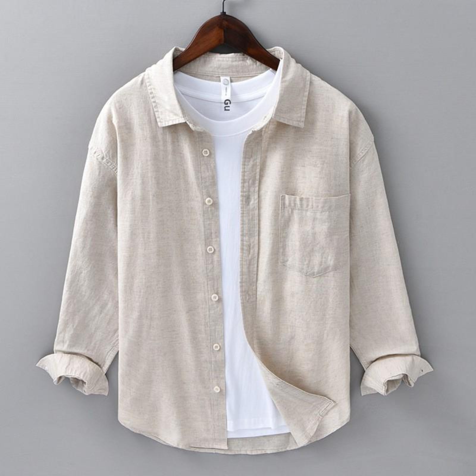Beige shirt over a white t-shirt on a hanger against a gray background